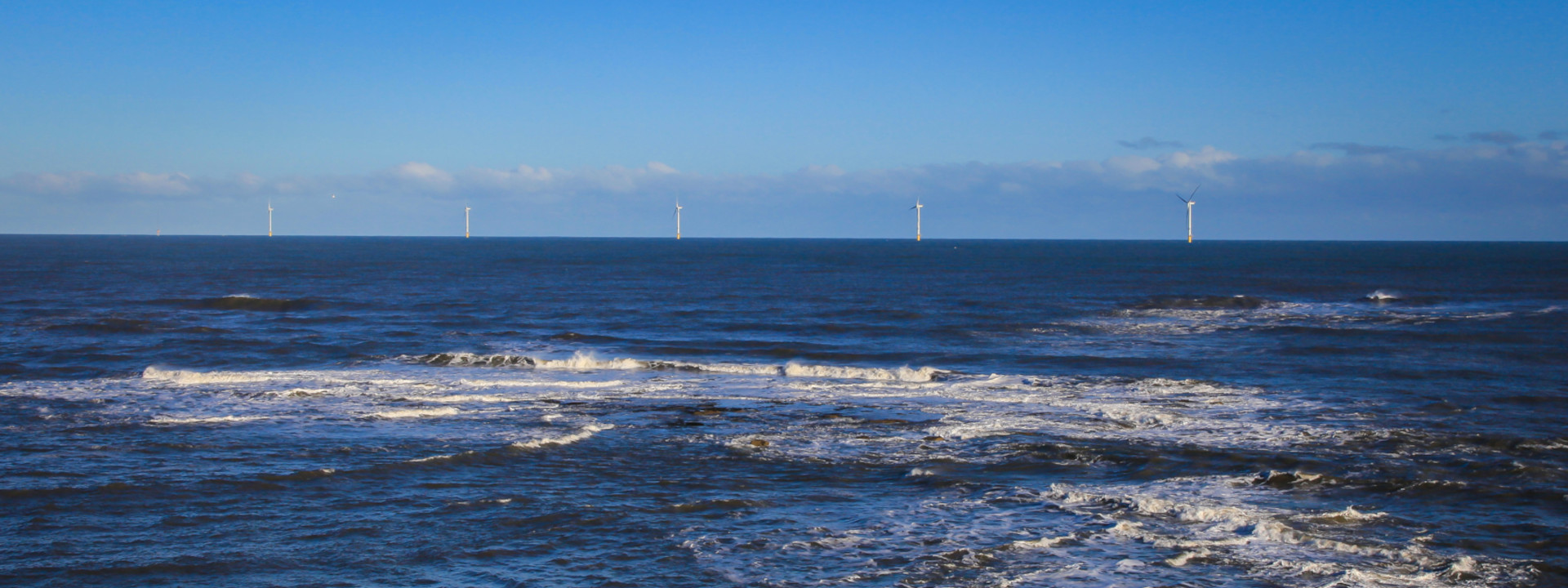 5 offshore wind turbines, the sea is breaking against an unseen shore